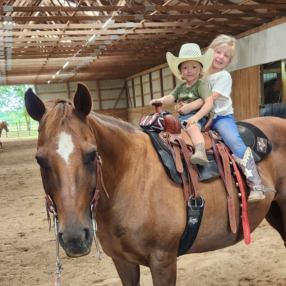 Two young riders sharing a saddle in the arena